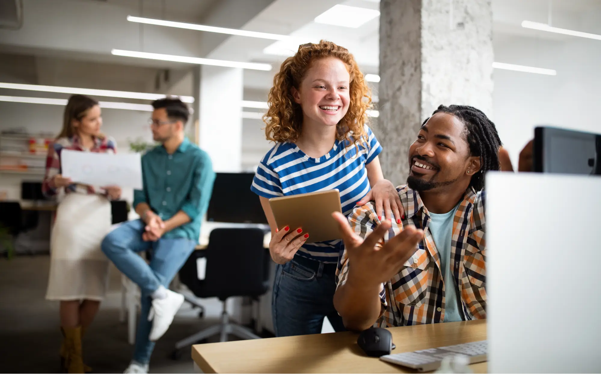 Two diverse co-workers working together on a digital tablet and laptop in an office