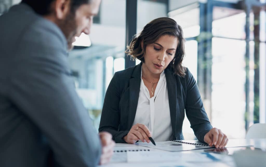 Woman in an office sitting at a desk beside a man, reviewing papers and talking